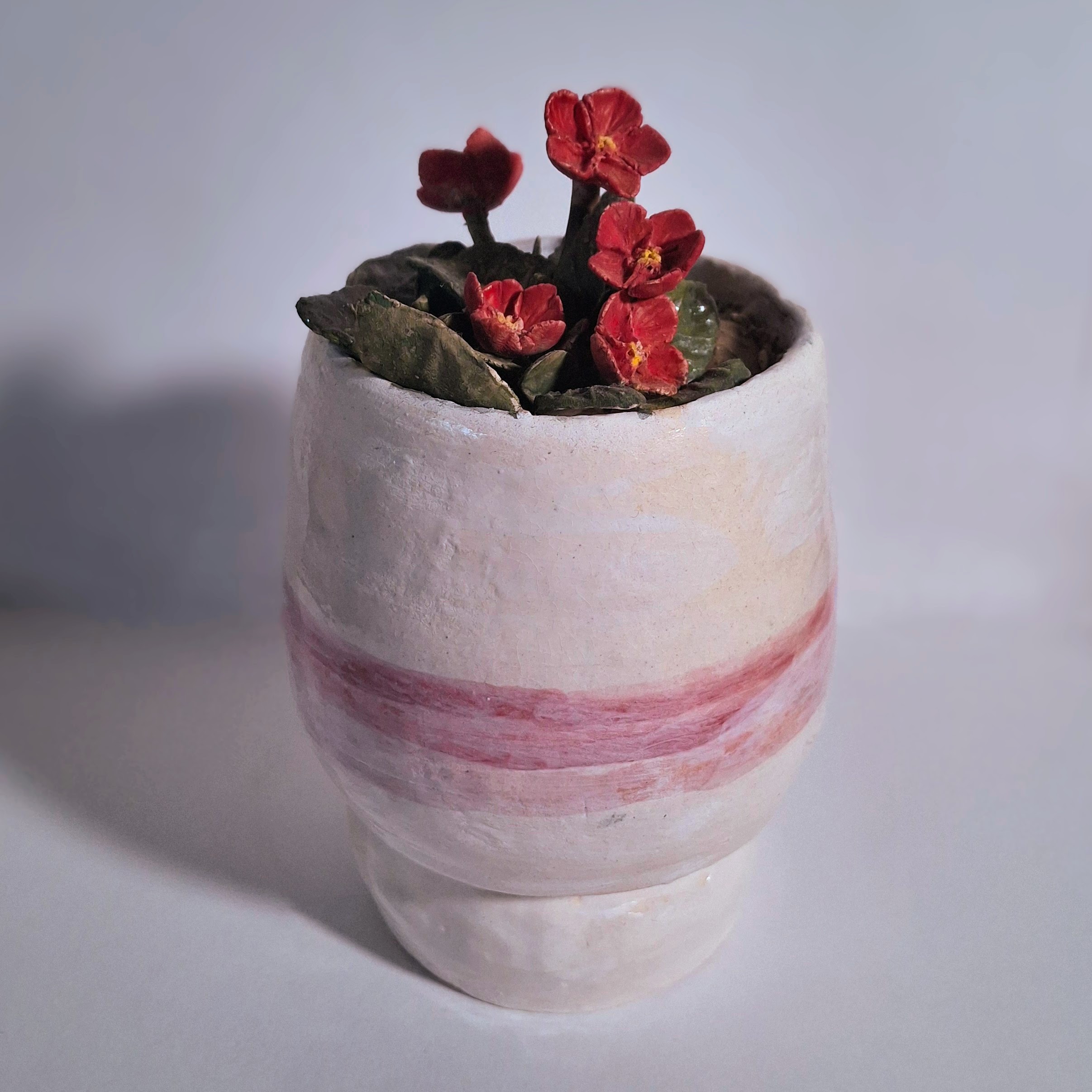 A ceramic sculpture of a small white pot and flowering red plant.