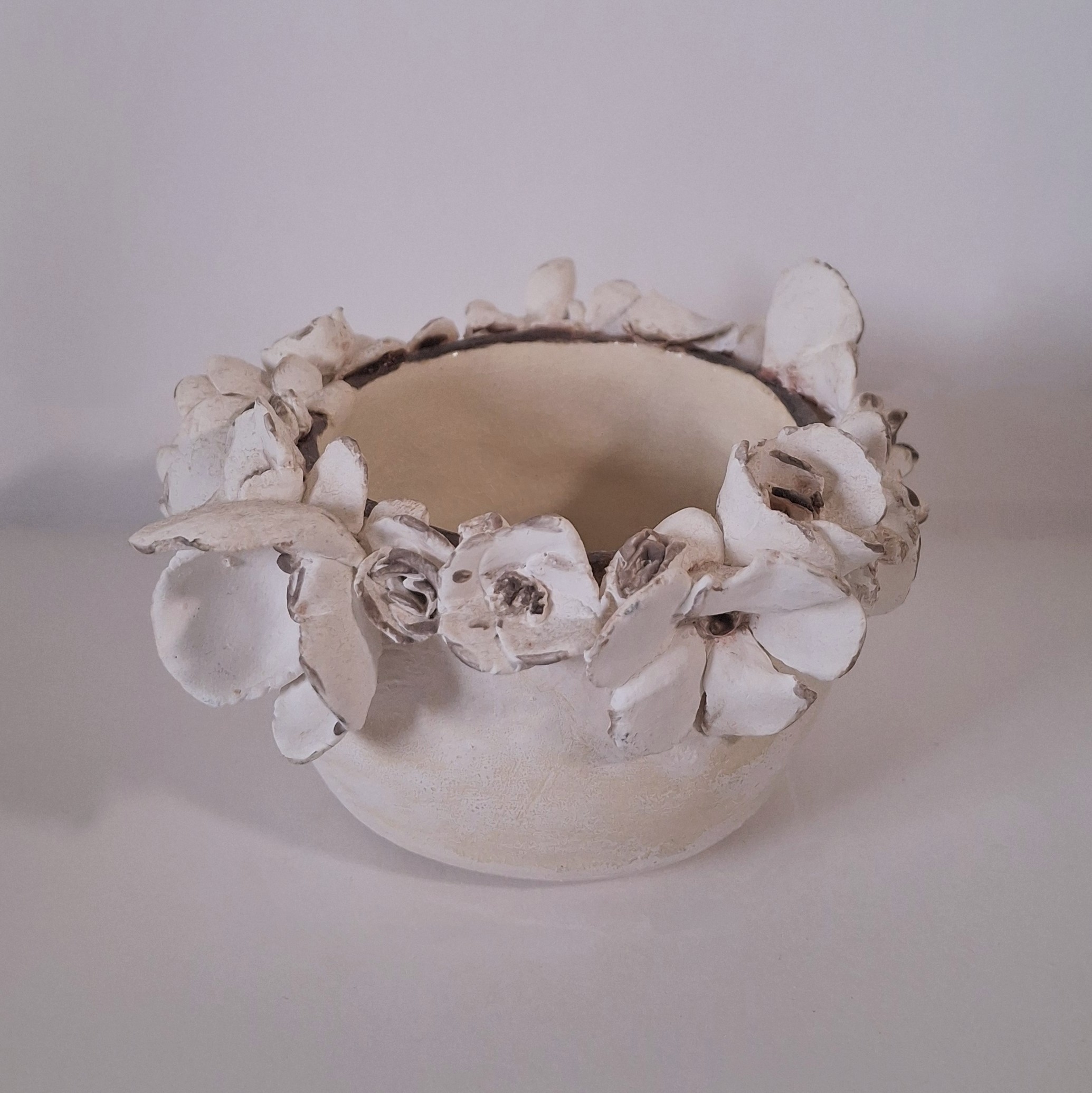 A small white ceramic cup surrouned by ceramic flowers along the rim.