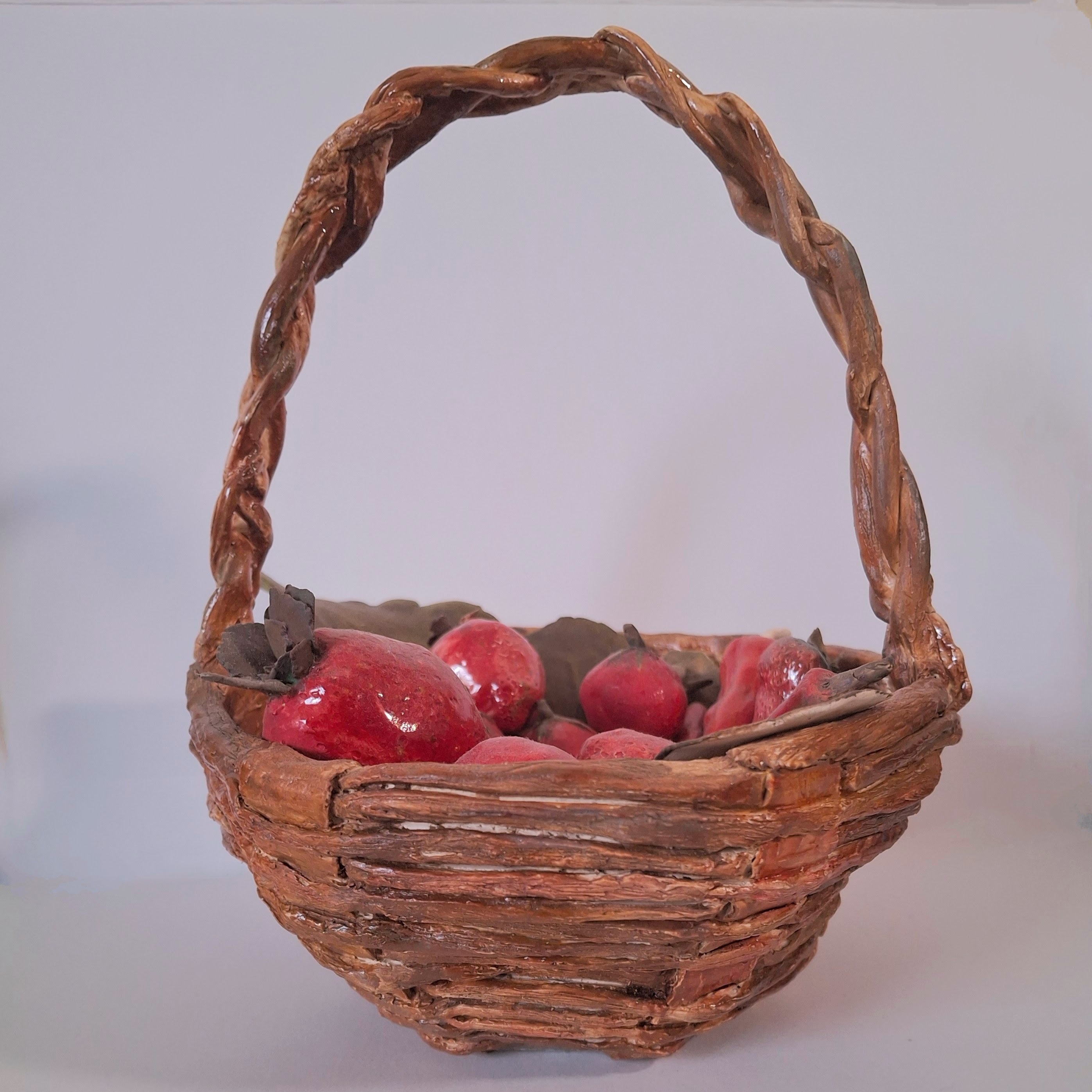 A ceramic sculpture of a woven brown basket filled with red fruit.