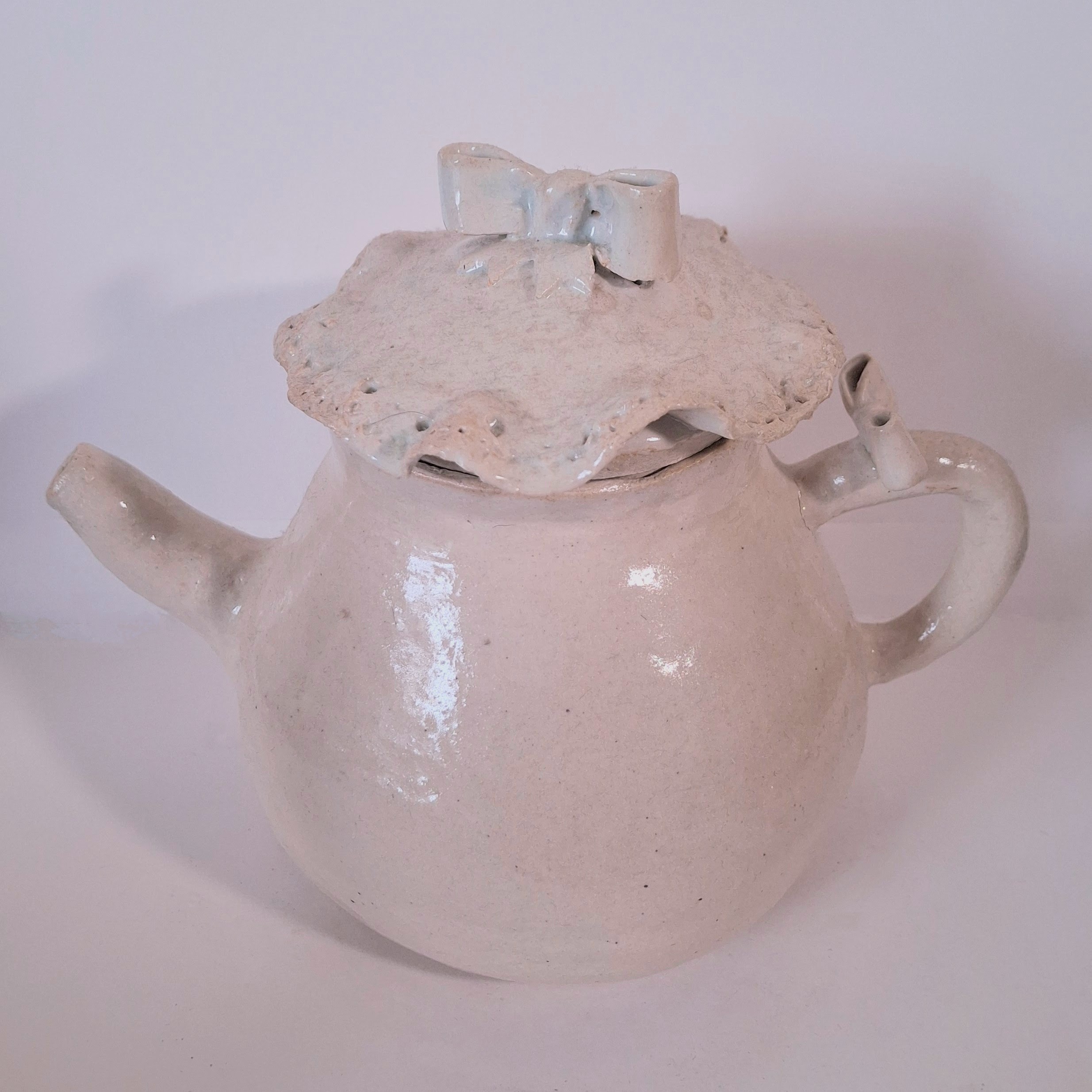 A round white teapot with a lacy design along the lid.