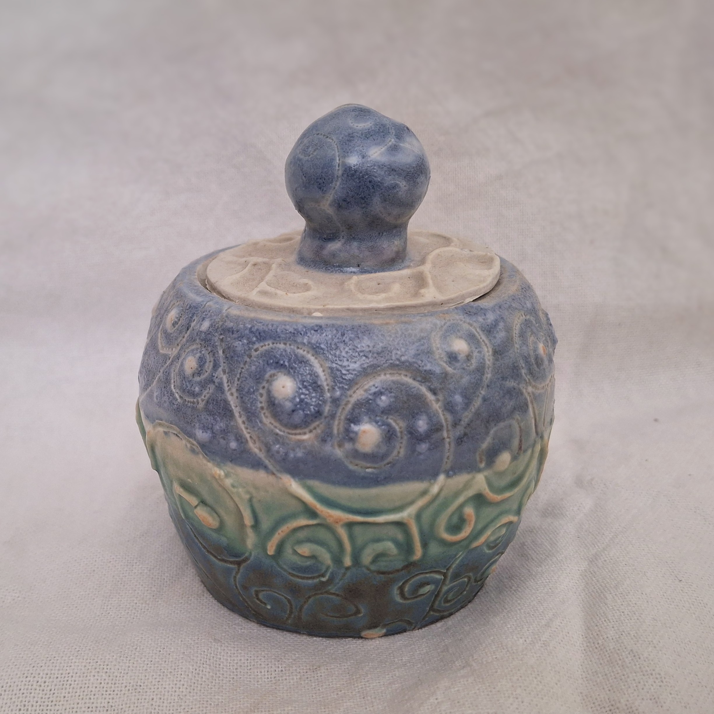 A small blue, green, and white ceramic jar